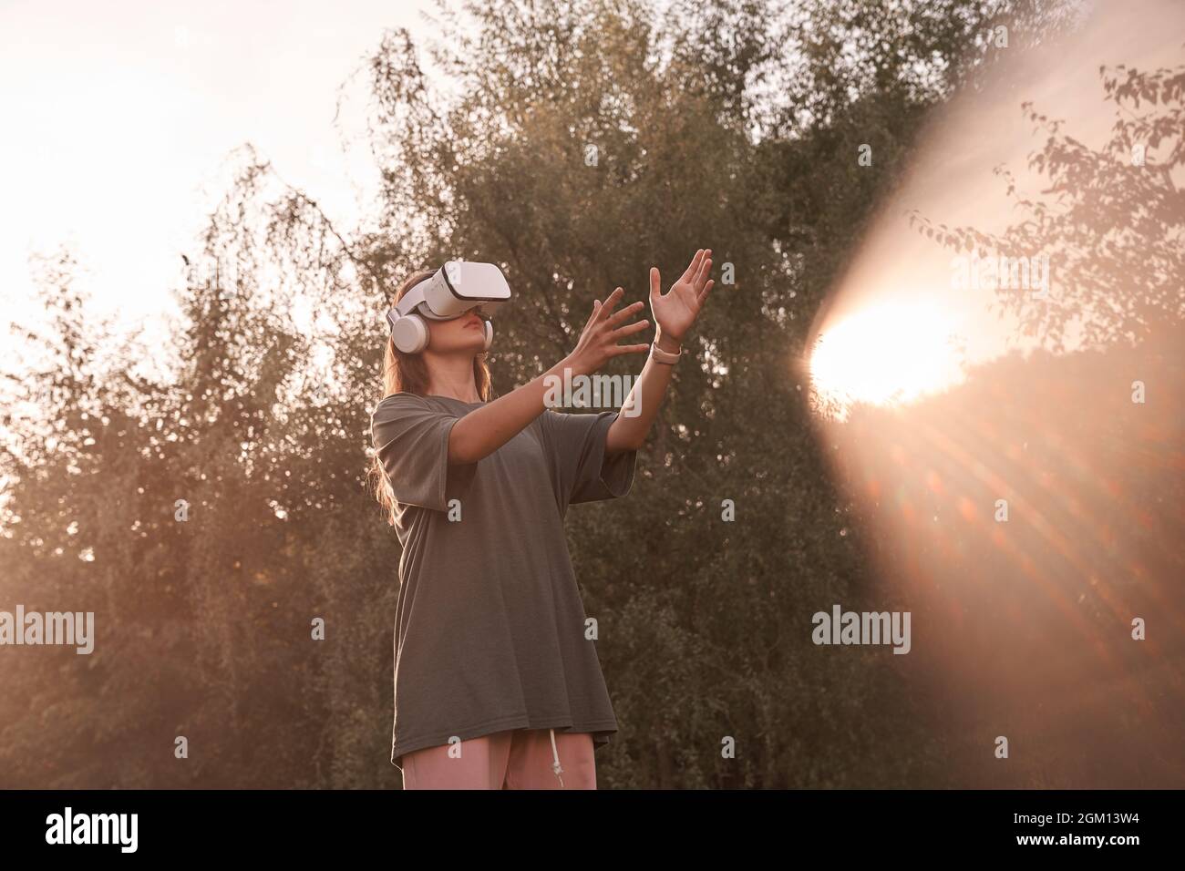 Ein Mädchen mit einer Virtual-Reality-Brille. Er reicht seine Hände an den Sonnenstrahl. Hochwertige Fotos Stockfoto