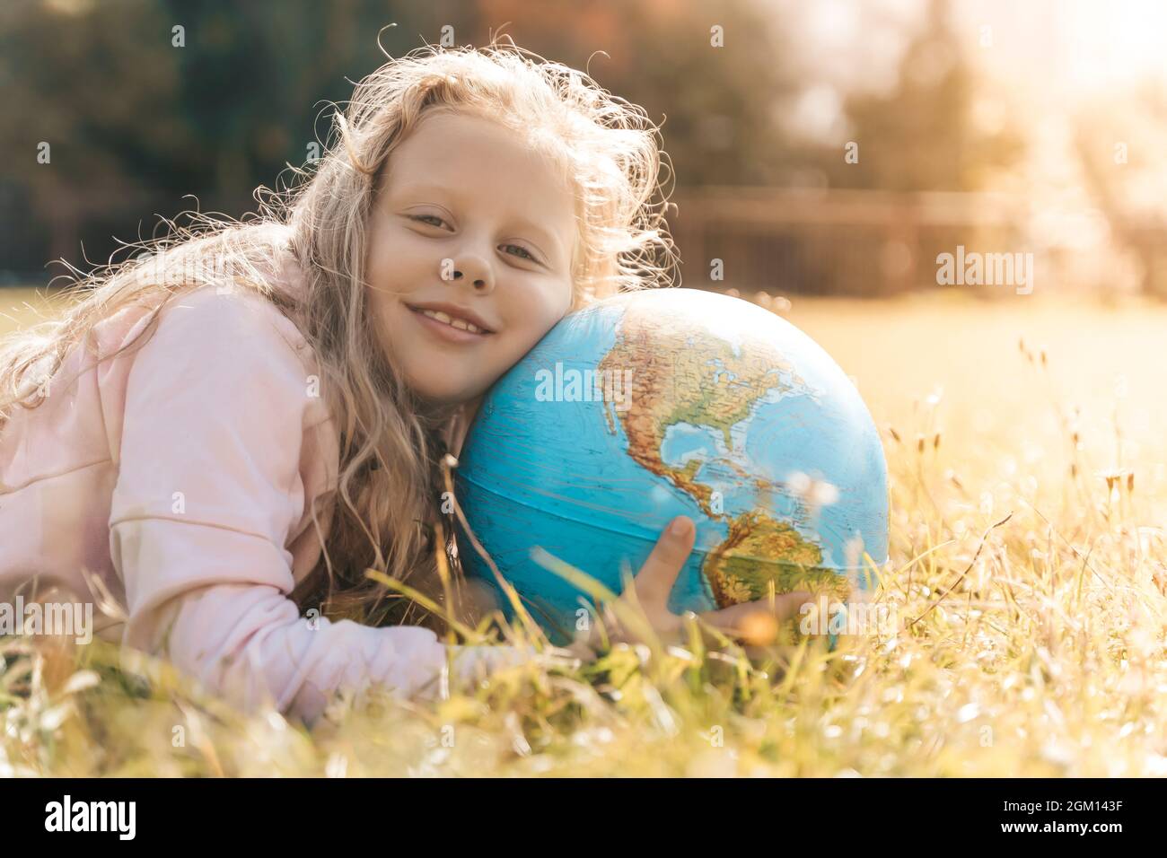 Kind mit Erdkugel. Porträt eines blonden europäischen Mädchens der Grundschule mit einem pädagogischen Globus des Planeten Erde in der Natur bei sonnigem Wetter. Konzept für Studium, Bildung, Naturschutz und Umweltschutz. Hochwertige Fotos Stockfoto