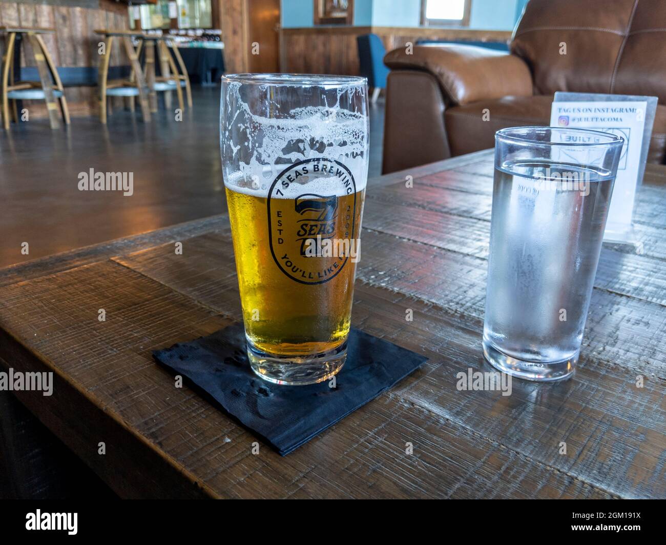 Tacoma, WA USA - ca. August 2021: Blick auf ein schaumiges Pilsner-Bier auf einem rustikalen Tisch in der 7 Seas Brewery Stockfoto