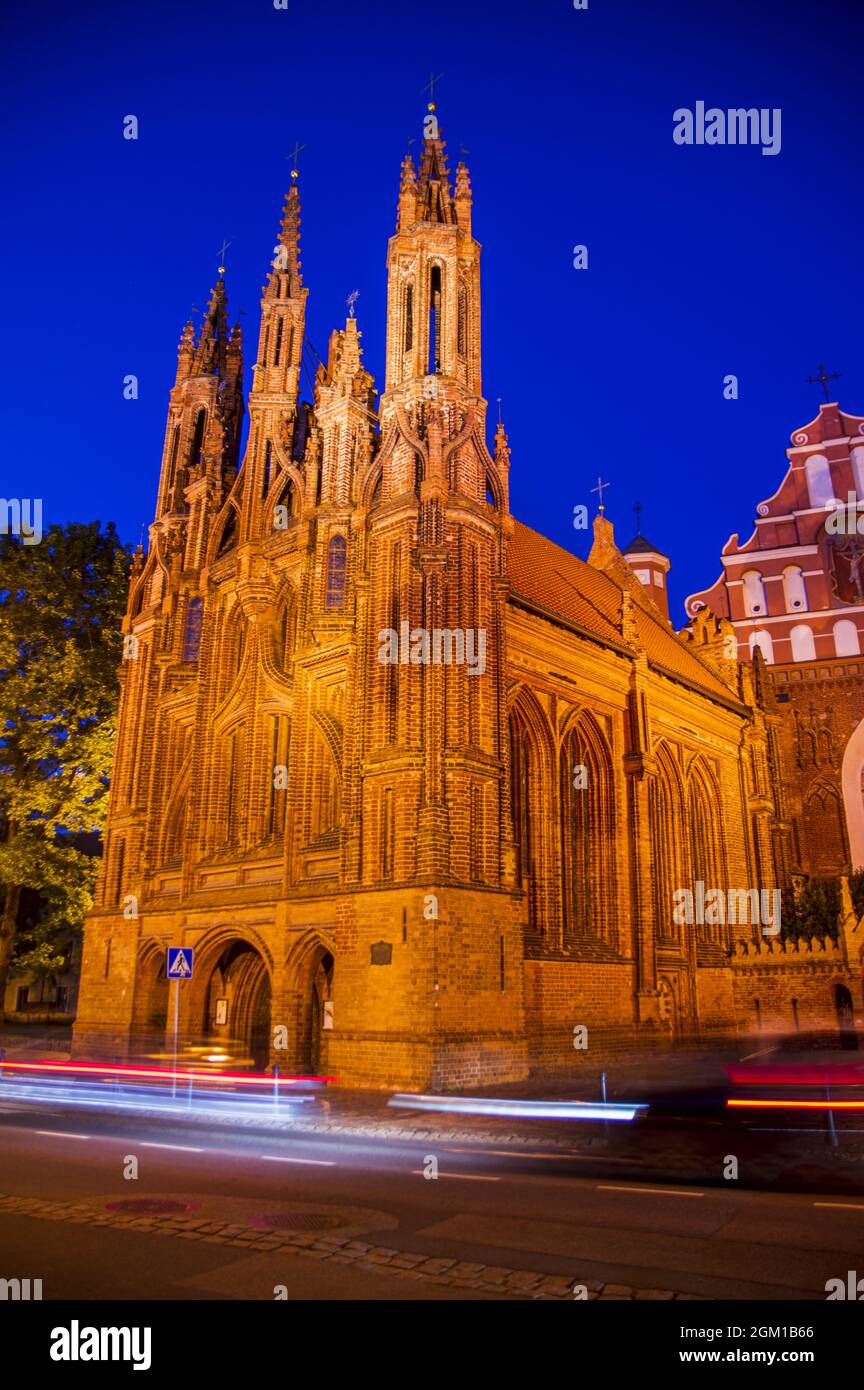 Beleuchtete schöne alte orthodoxe Kirche in der Altstadt von Vilnius. Gebäude mit gotischen Türmen an der Hauptstraße der Stadt in der Nacht nach Sonnenuntergang mit den Lichtwegen. Die Bewegung des Autos verwischt Stockfoto