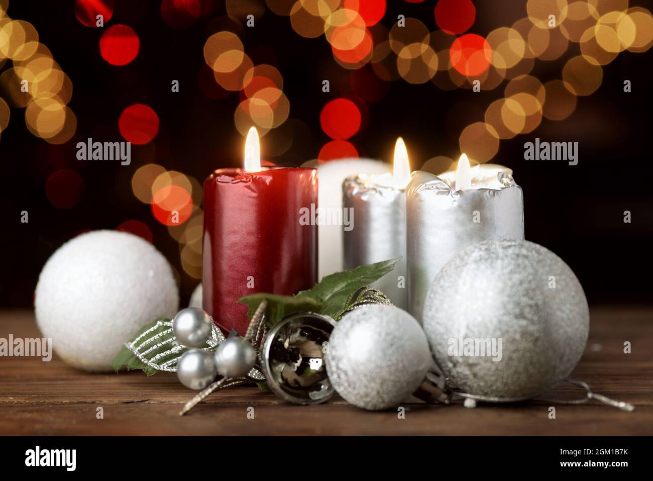 Brennende Weihnachtskerzen und Ornamente über verschwommenen festlichen Lichtern auf dunklem Hintergrund Stockfoto