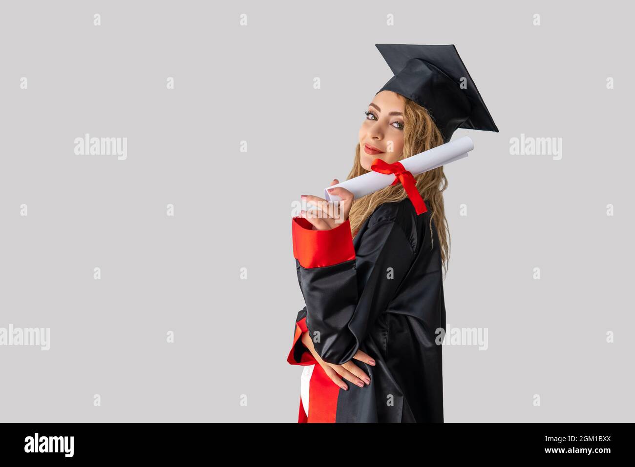 Eine hübsche Studentin, die ihren Abschluss feiert und vor einer weißen Wand steht und ihr Diplom mit Erfolg hält. Hochwertige Fotos Stockfoto
