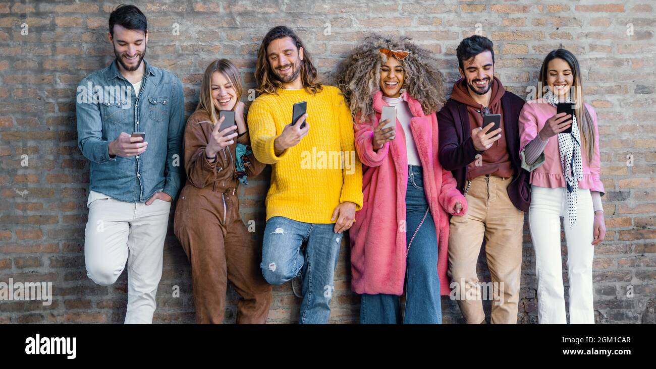 Eine Gruppe von jungen Menschen, die sich mit Smartphones scherzen und online Inhalte sozialer Netzwerke durchsuchen, die sich gegen eine Mauer erheben. Technolo Stockfoto