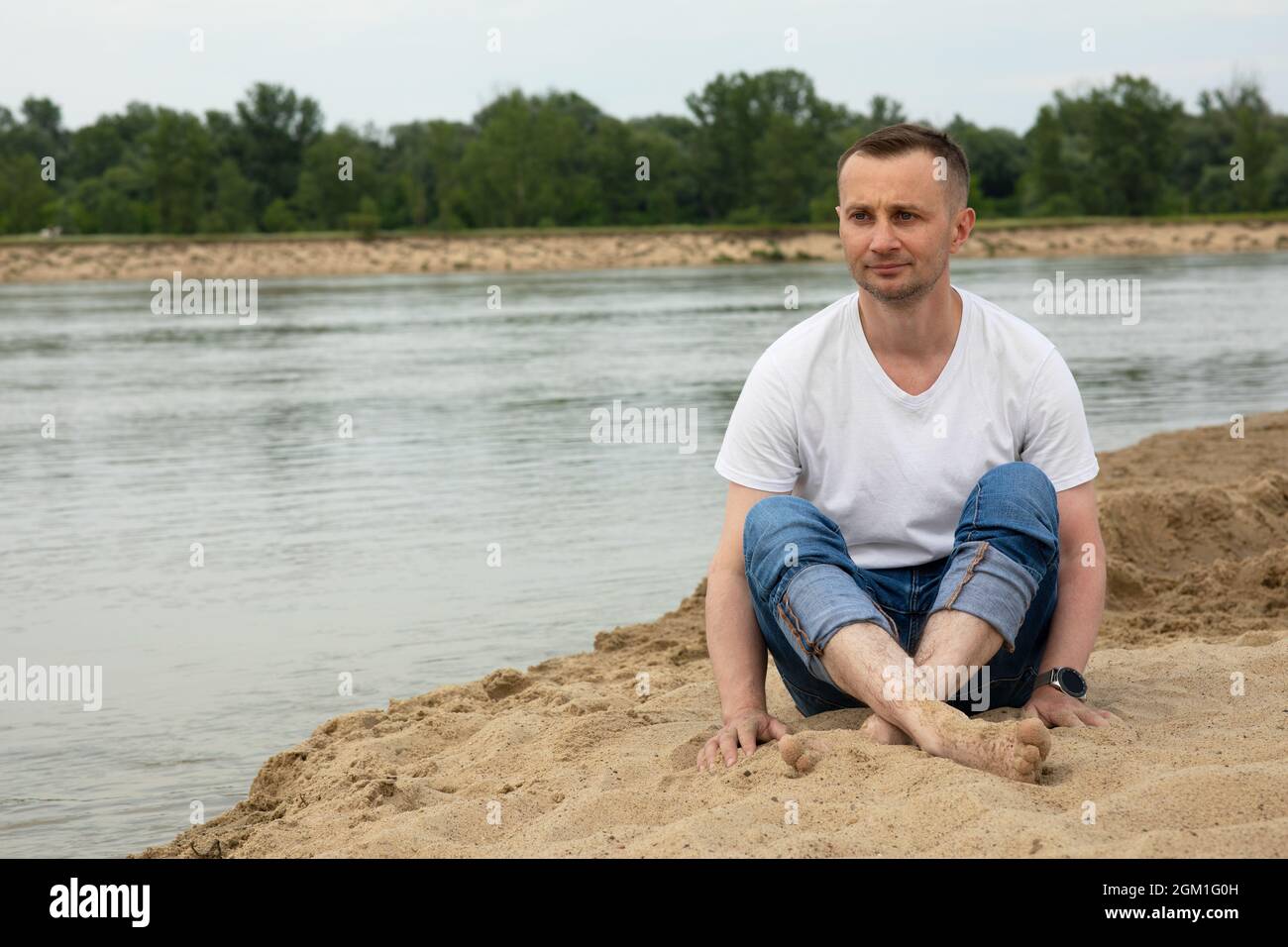 Das Bild einsam positiv und lächeln Mann sitzt am Strand Fluss Stockfoto