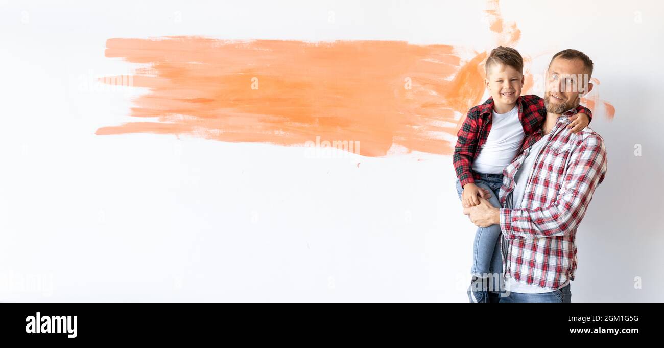 Glückliche junge Familie renoviert ihr Haus. Vater hält seinen Sohn in den Armen. Weiße Wand im Raum mit Platz für Text. Stockfoto