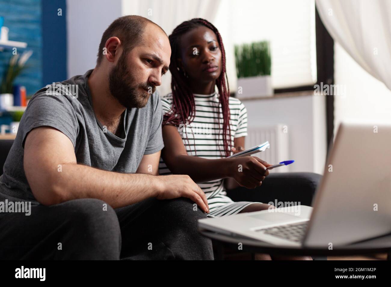 Interracial paar mit Laptop für Steuern Zahlung und Wirtschaft zu Hause. Menschen mit gemischter Rasse, die Finanzbudget und Steuergelder in Rechnung gestellt haben, während das Gerät mit Technologie verwendet wird. Stockfoto