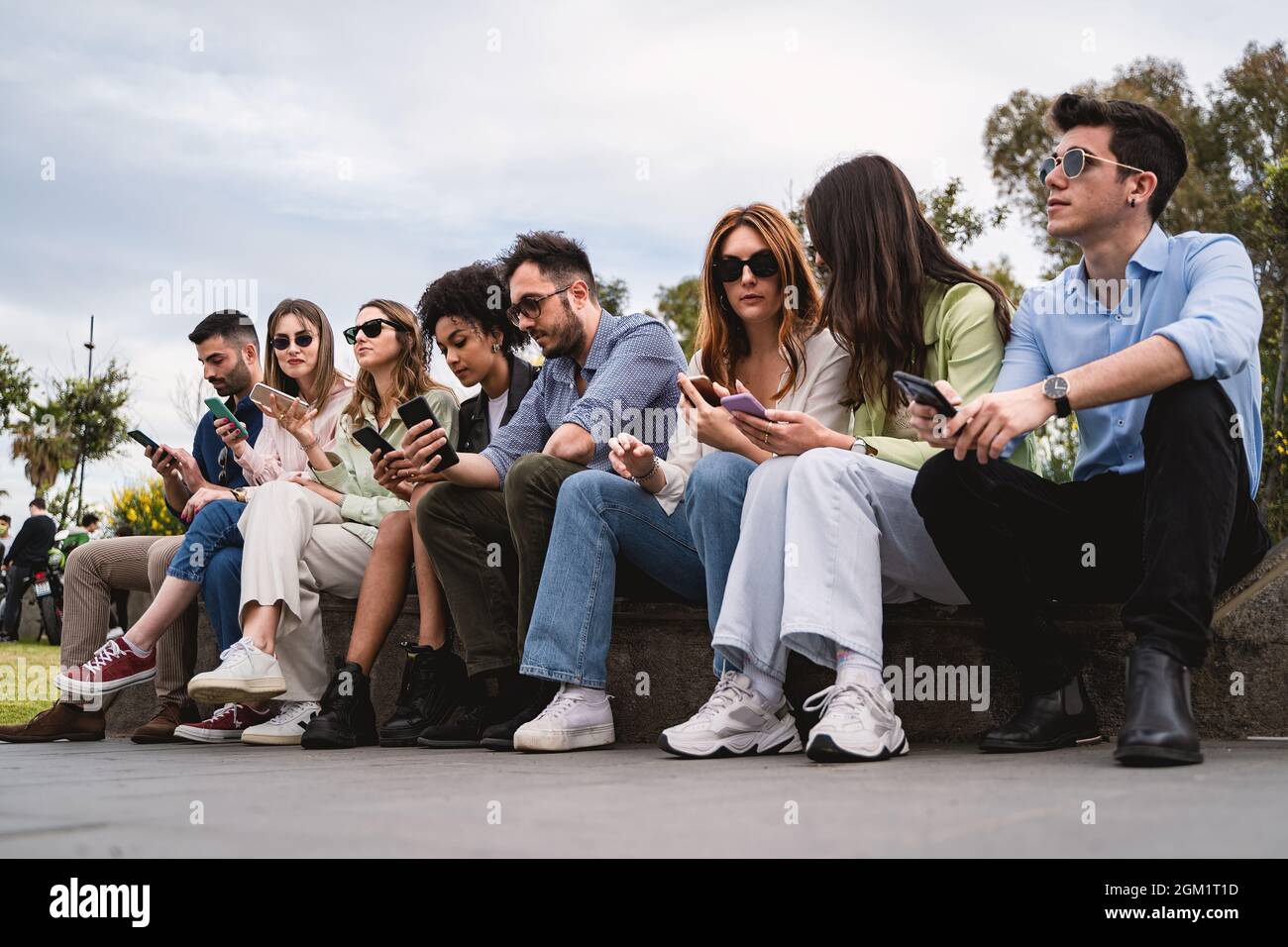 Generation z Jugendliche sitzen auf einer Bank und nutzen Smartphone. Konzept von jungen Menschen, die von Technologie und sozialen Netzwerken abhängig sind. Stockfoto