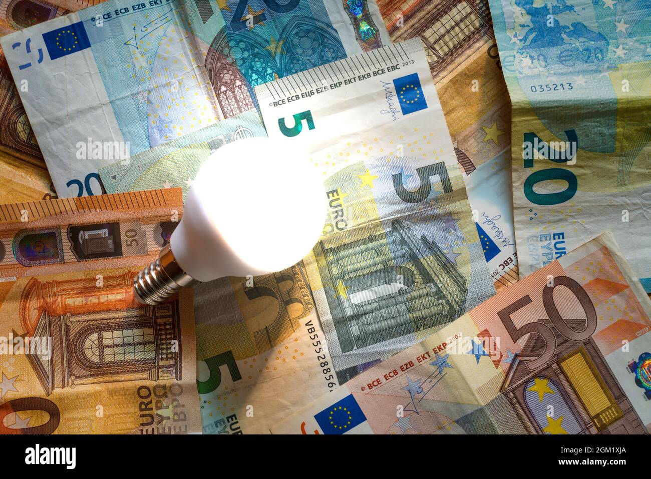 Glühbirne auf einem Hintergrund von Euro-Banknoten. Konzept der steigenden Strompreise. Stockfoto