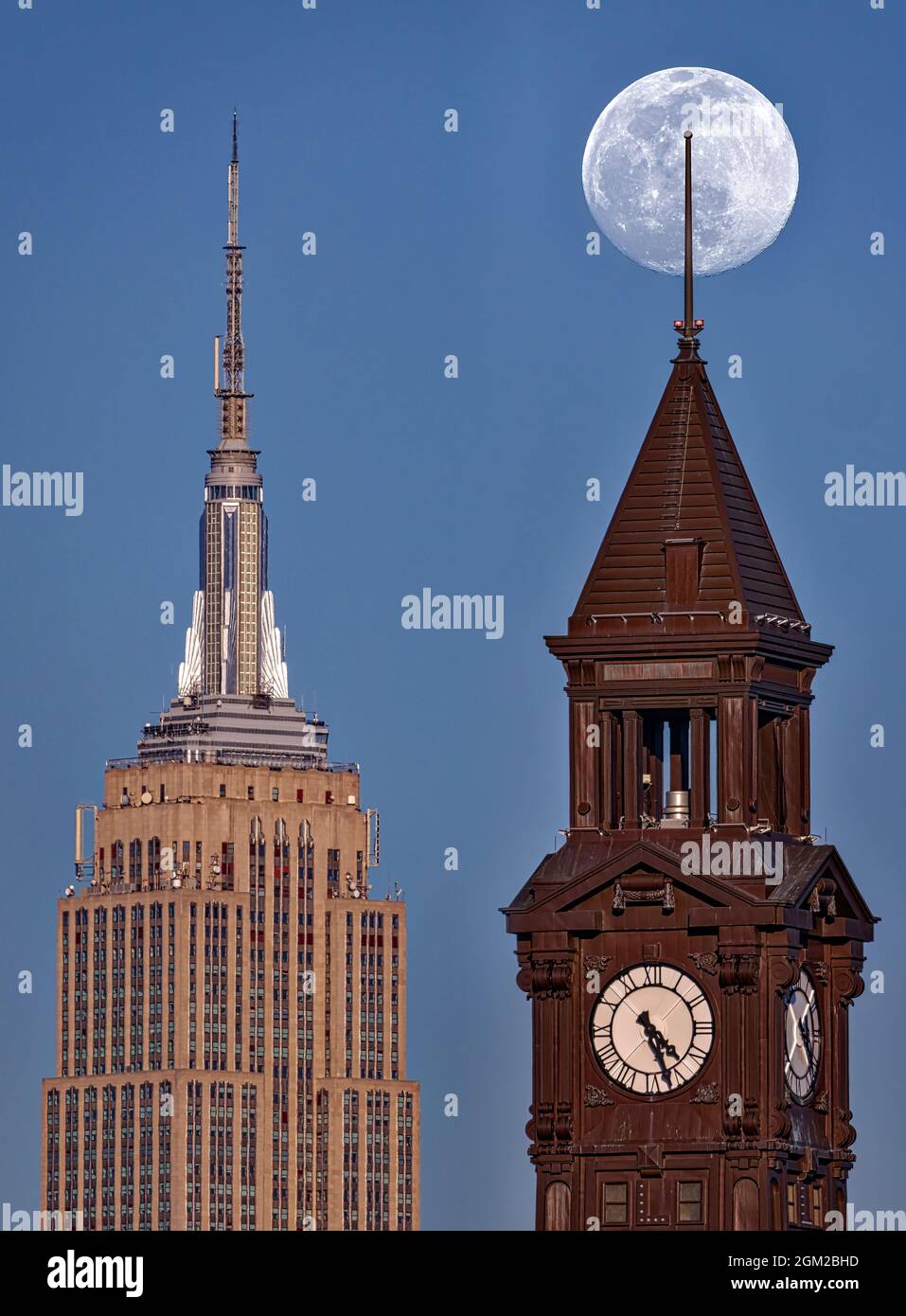 NY NJ Crossing State Lines der fast volle Schneemond erhebt sich hinter dem Lackawanna Clock Tower in Hoboken, New Jersey, und dem Empire State Building in N Stockfoto
