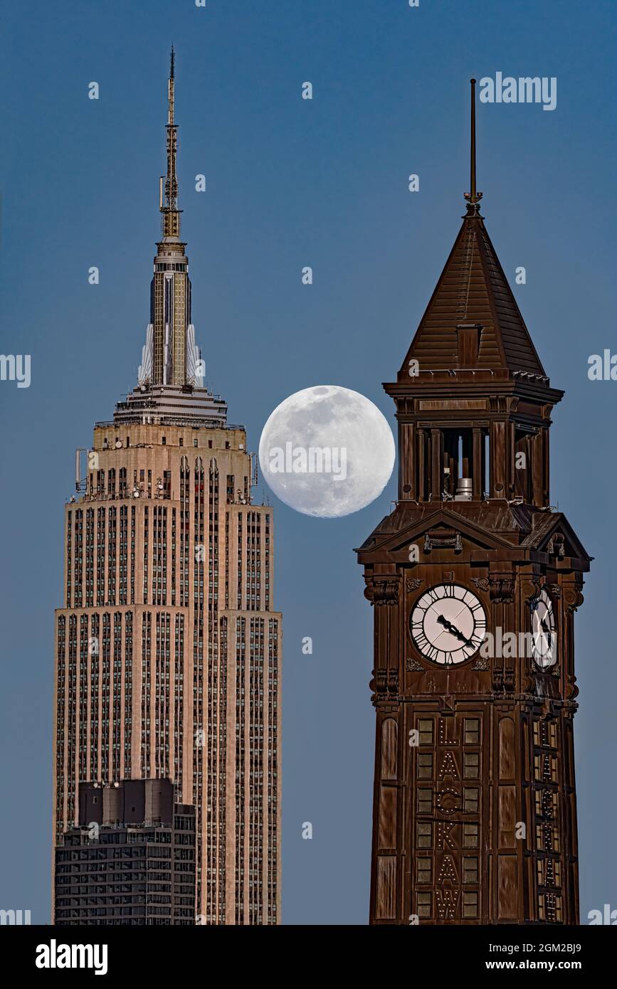 NJ NYC Crossing State Lines - der volle Schneemond erhebt sich zwischen dem Lackawanna Clock Tower in Hoboken, New Jersey, und dem Empire State Building in New York Stockfoto