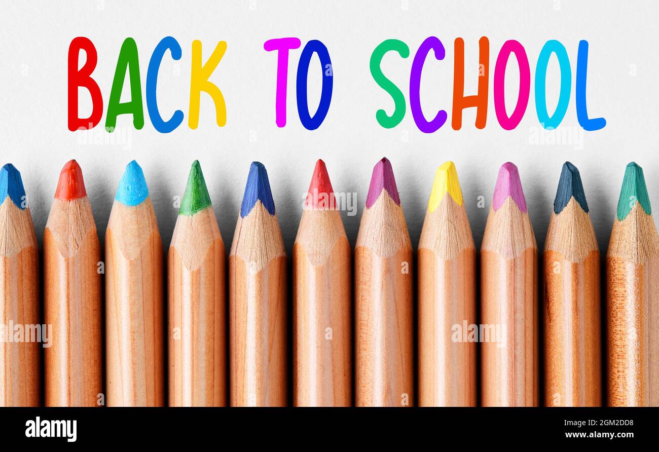 Bunte Holzkreidestifte in einer Reihe mit einer Nachricht von der Schule, die mit bunten Buchstaben an der Spitze geschrieben wurde. Stockfoto