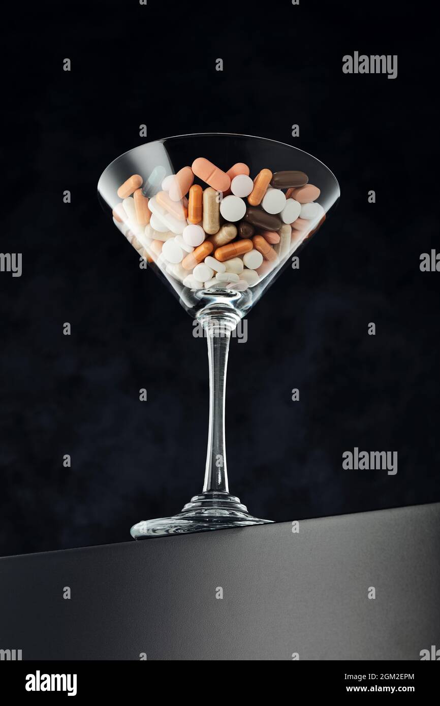 Cocktailglas gefüllt mit bunten medizinischen Pillen. Drogenabhängigkeit, Überkonsum, medizinische Behandlung oder Rezept-Konzept der Gesundheitsbranche. Stockfoto