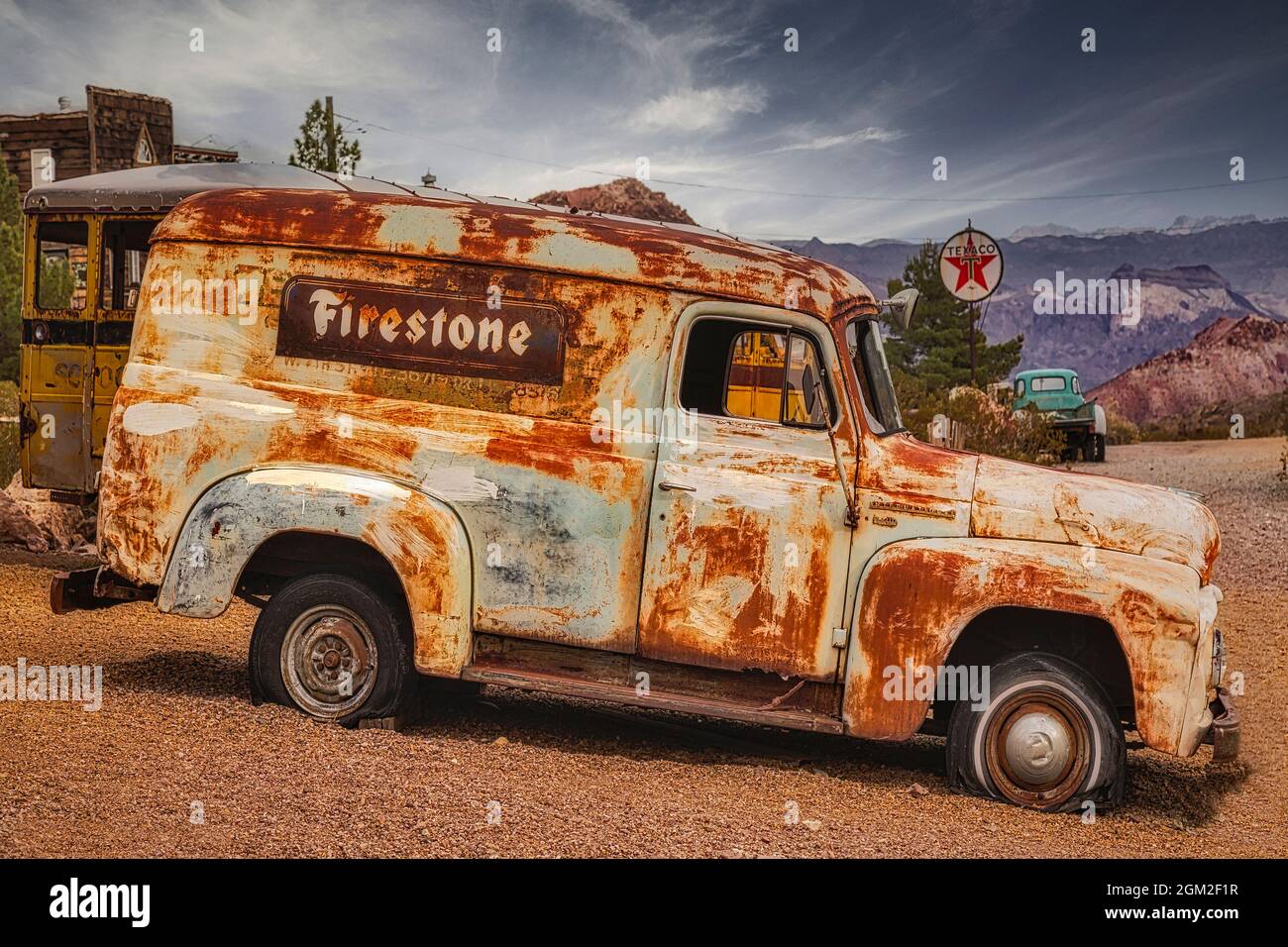 Firestone Truck - Ein alter verlassener und verwitterter Firestone Truck mit einer Texaco Tankstelle mit antikem Pick-up Truck im Hintergrund. Stockfoto