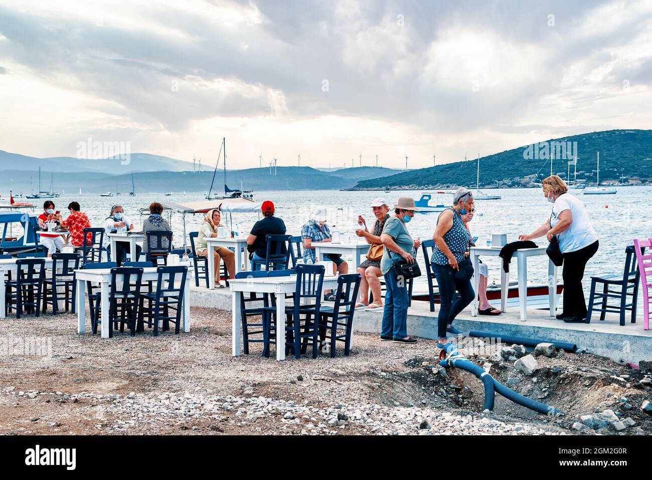 Juni 2021 - Seferihisar, Izmir, Türkei: Menschen sitzen in den Cafés am Meer am Seferihisar Hafen in Izmir, Türkei. Stockfoto