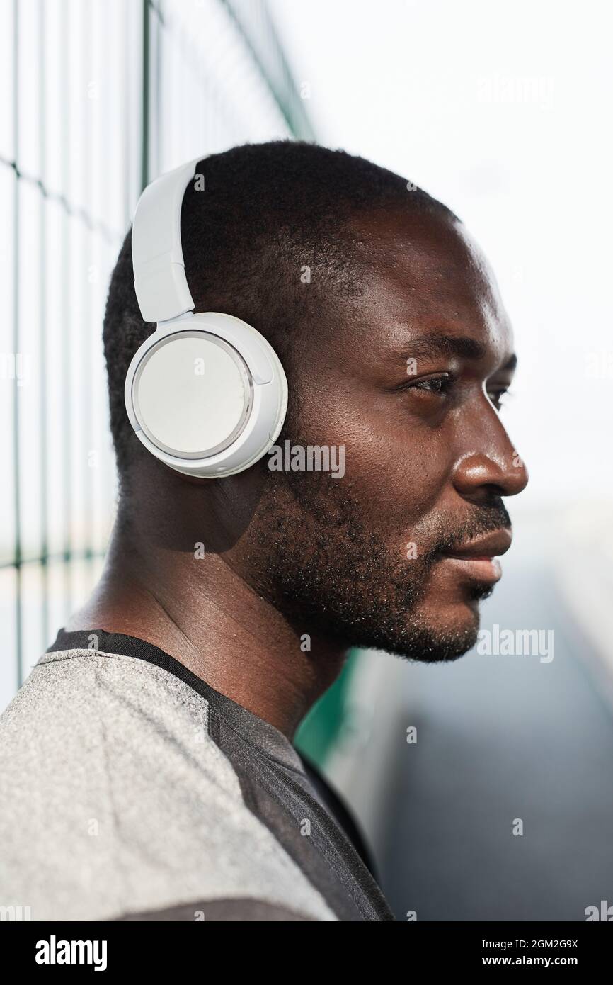 Seitenansicht eines afrikanischen jungen Mannes in kabellosen Kopfhörern, der Musik hört, während er im Freien steht Stockfoto