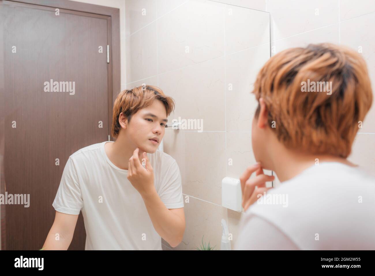 Junger Mann, der vor dem Spiegel steht und sein Gesicht berührt Stockfoto
