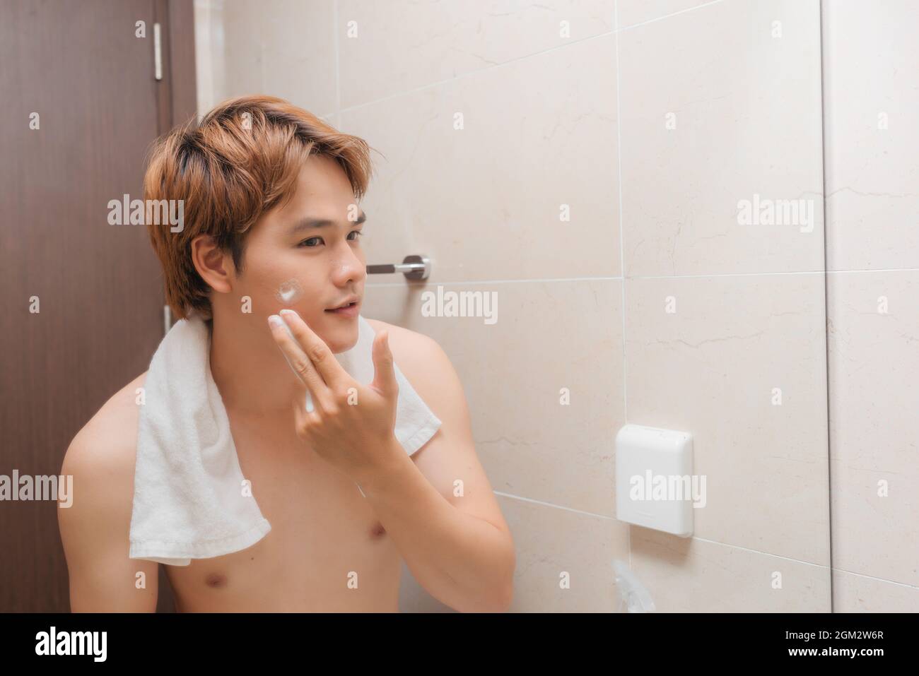 Porträt eines schönen lächelnden gesunden Mannes, der Schaum zum Waschen auf sein Gesicht aufschäumt. Stockfoto
