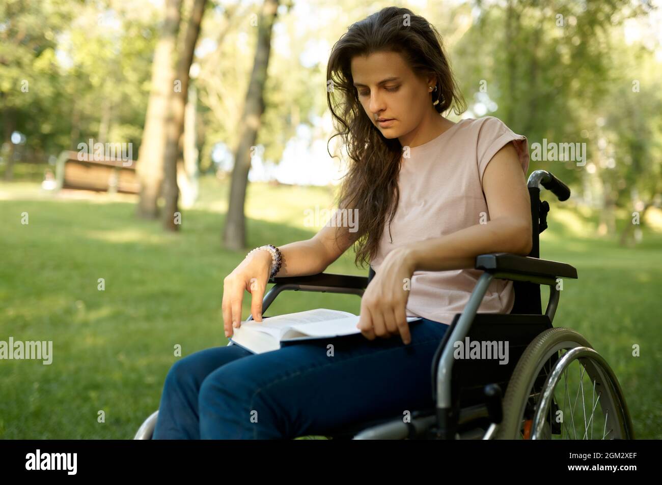 Eine behinderte Frau im Rollstuhl liest im Park ein Buch Stockfoto