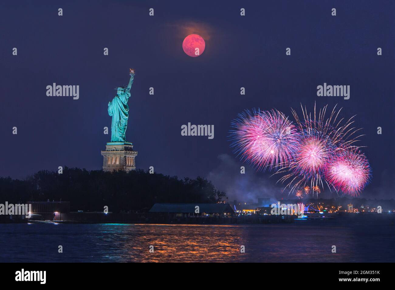 Freiheitsstatue Mondaufgang - der Supermond steigt während der blauen Stunde nach Sonnenuntergang über der Freiheitsstatue auf. Im Hintergrund ist ein Feuerwerk zu sehen Stockfoto