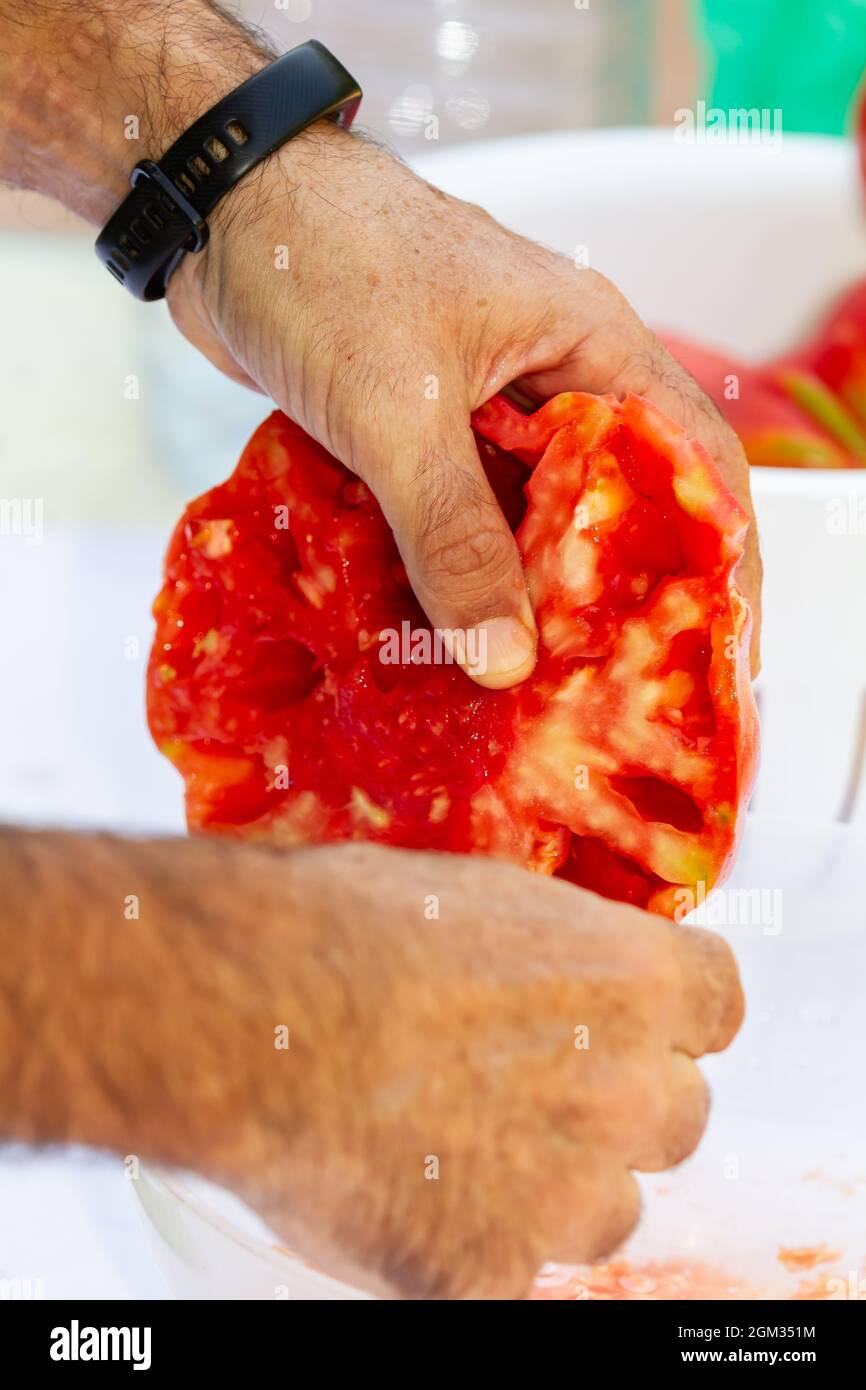 Hände eines Mannes, der eine halbiert geschnittene Tomate putzt Stockfoto