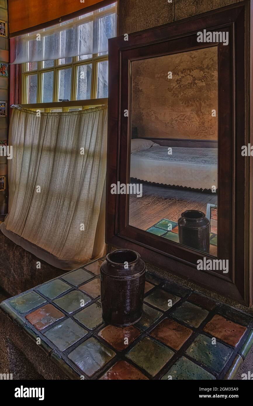 Schlafzimmer Reflexionen - Ein Einzelbett spiegelt sich in einem Spiegel im eklektischen Schloss wider. Der Spiegel sitzt auf einem Tisch, der mit bunten Fliesen und nex bedeckt ist Stockfoto