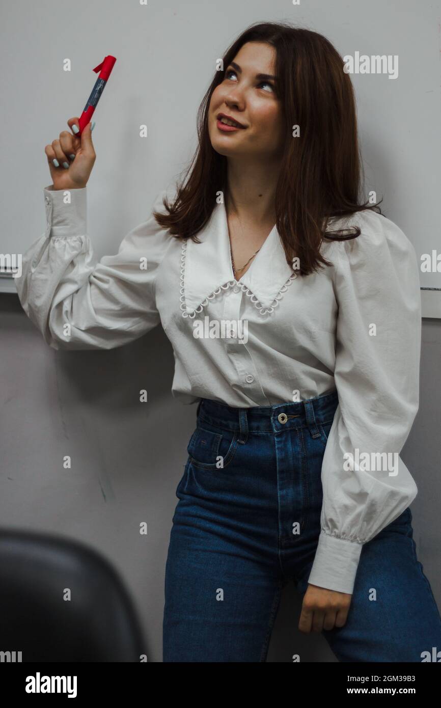 Junger Pädagoge in einer weißen Bluse mit einem roten Marker, der vor einem weißen Brett steht. Blickt in die Kamera. Stockfoto