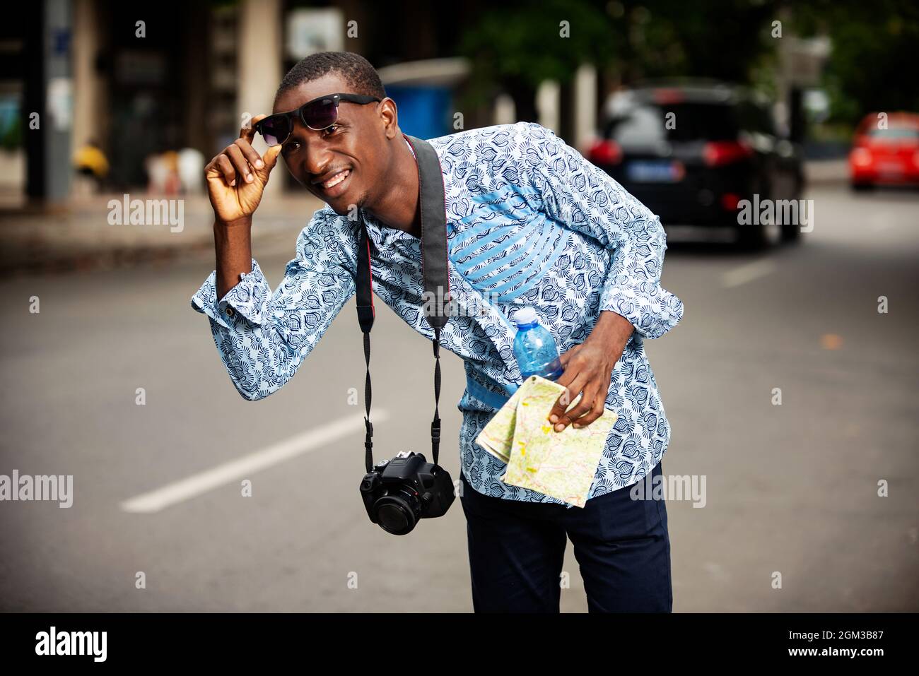 Fröhlicher junger Mann, der als Tourist auf die Straße schaut, während er seine Sonnenbrille aufhebt Stockfoto