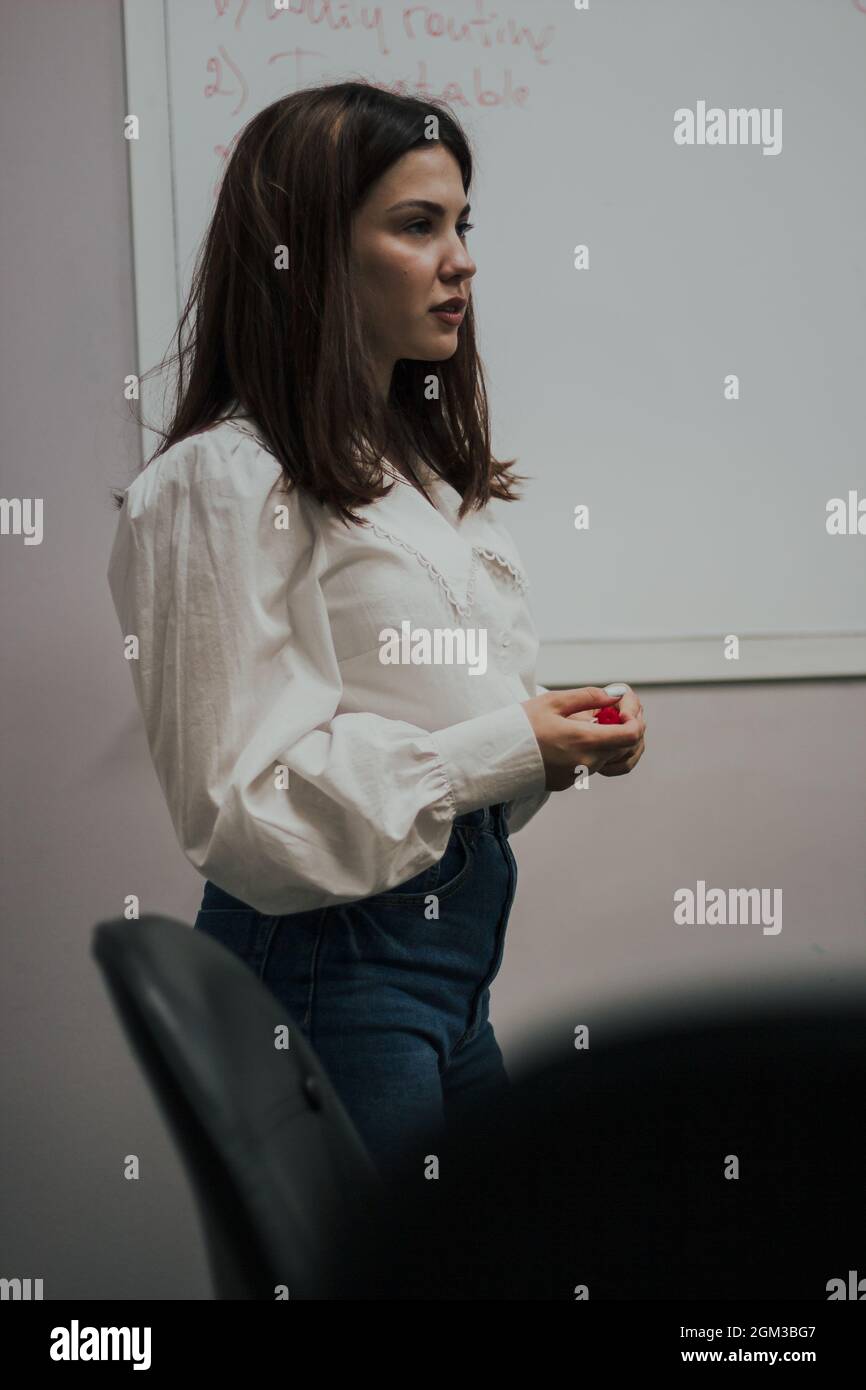 Junge Englischlehrerin mit einem roten Marker in einer weißen Bluse, die vor einem weißen Brett steht. Stockfoto