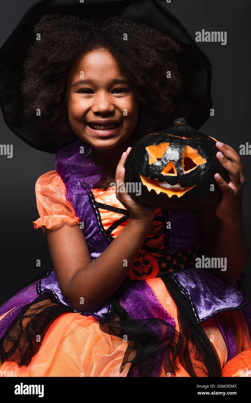 Happy african american Mädchen in spitzen Hut hält geschnitzten Kürbis isoliert auf schwarz Stockfoto