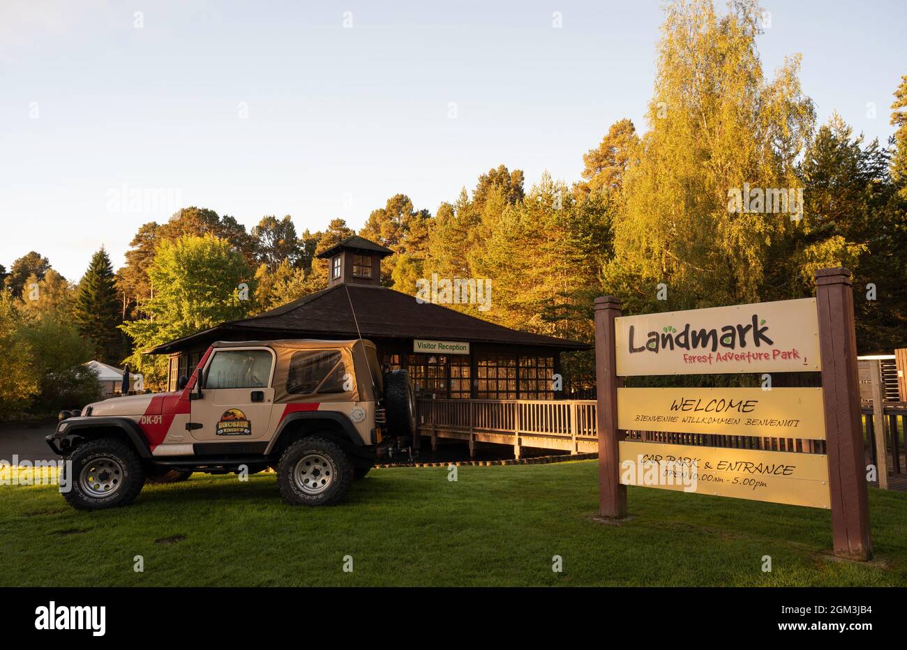 Schilder für Landmark Forest Adventure Park am Eingang mit Besucherempfang und Dinosaur Kingdom Jeep in Sicht. Bäume und blauer Himmel Hintergrund. Stockfoto