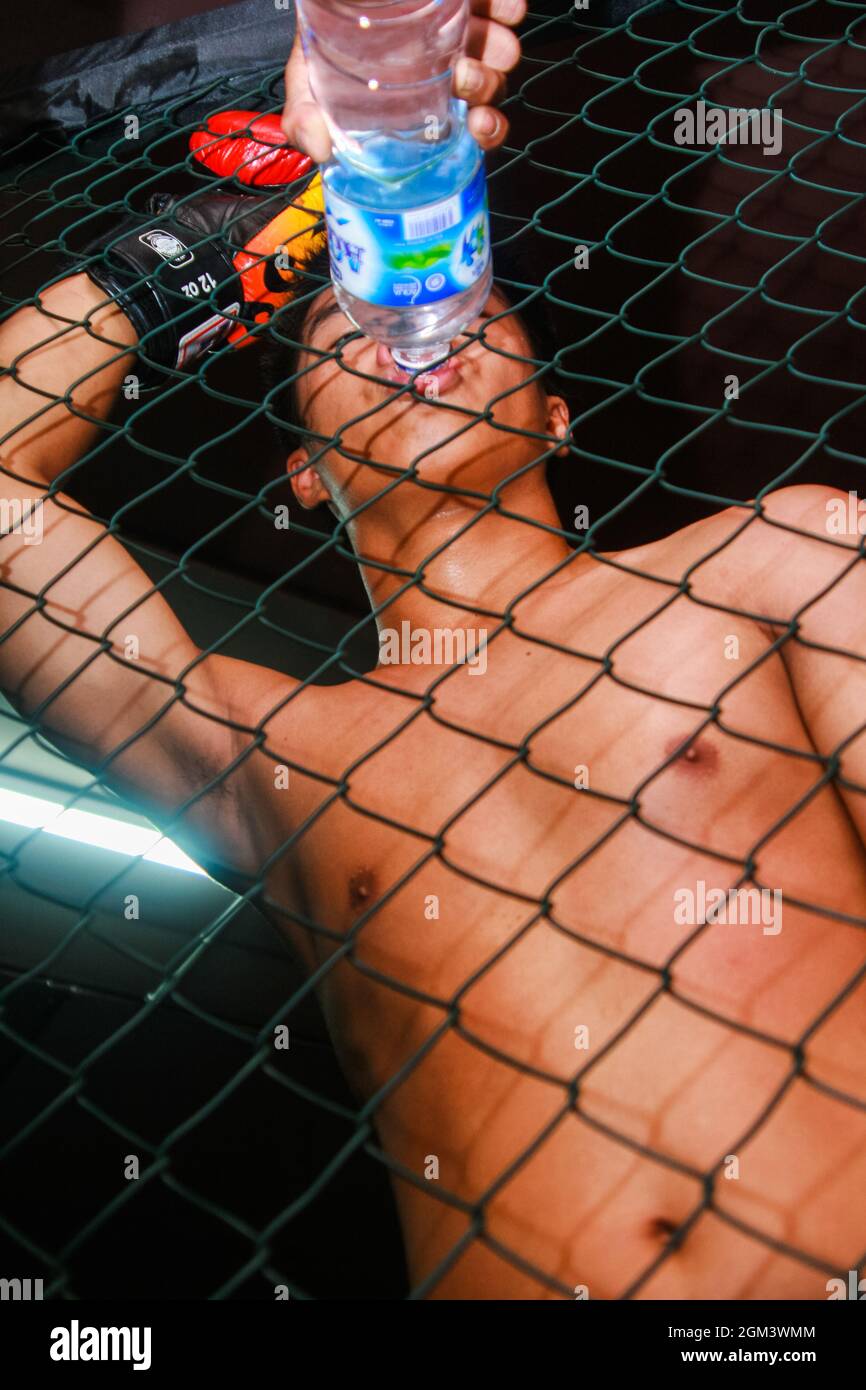 Ein Kämpfer der MMA (Mixed Martial Arts) trinkt Mineralwasser aus einer Flasche, die sein Trainer hinter einem Drahtkäfig herausstieß. Stockfoto