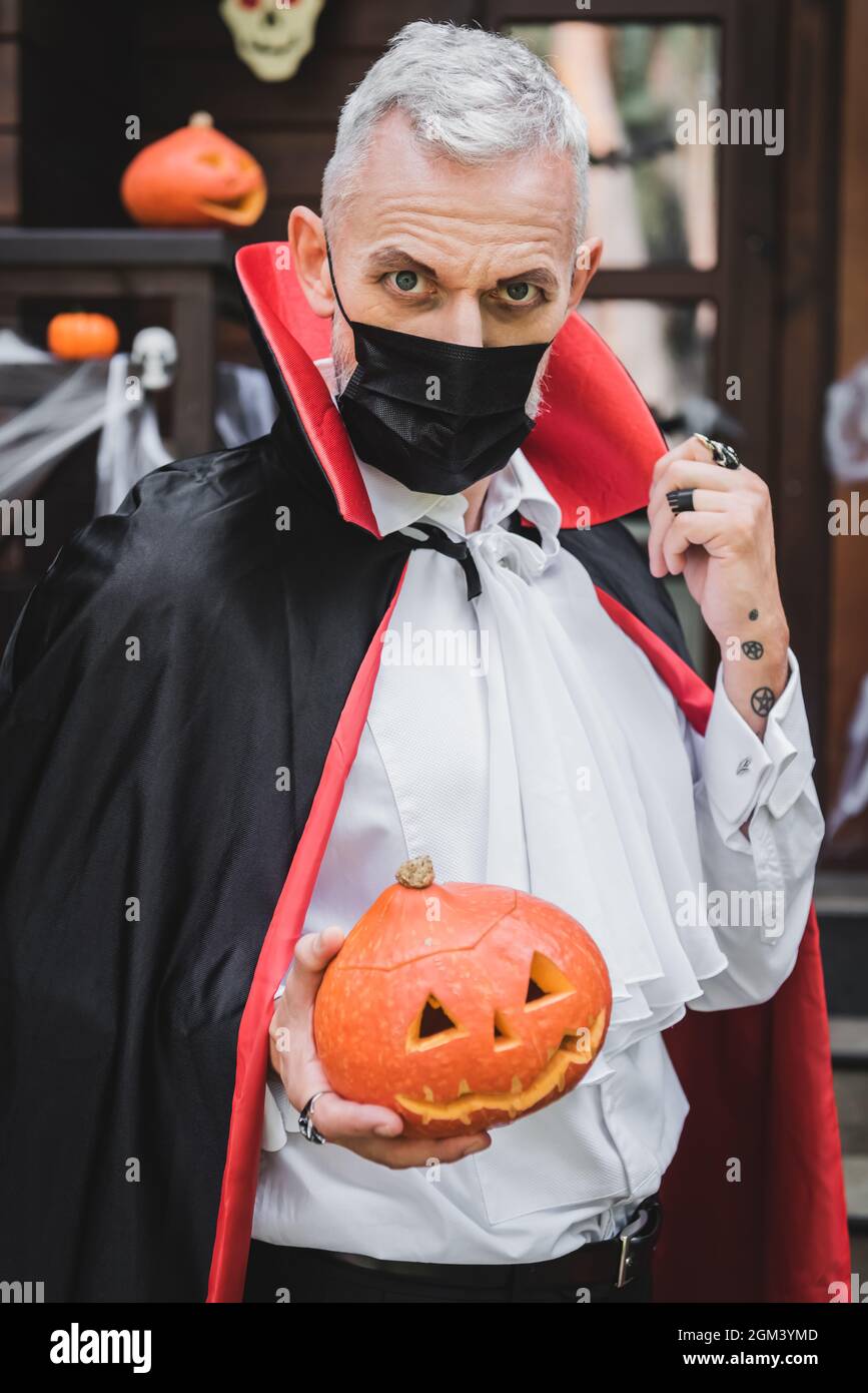 Mann mittleren Alters in schwarzer medizinischer Maske und Vampir halloween  Kostüm mit geschnitztem Kürbis beim Blick auf die Kamera Stockfotografie -  Alamy