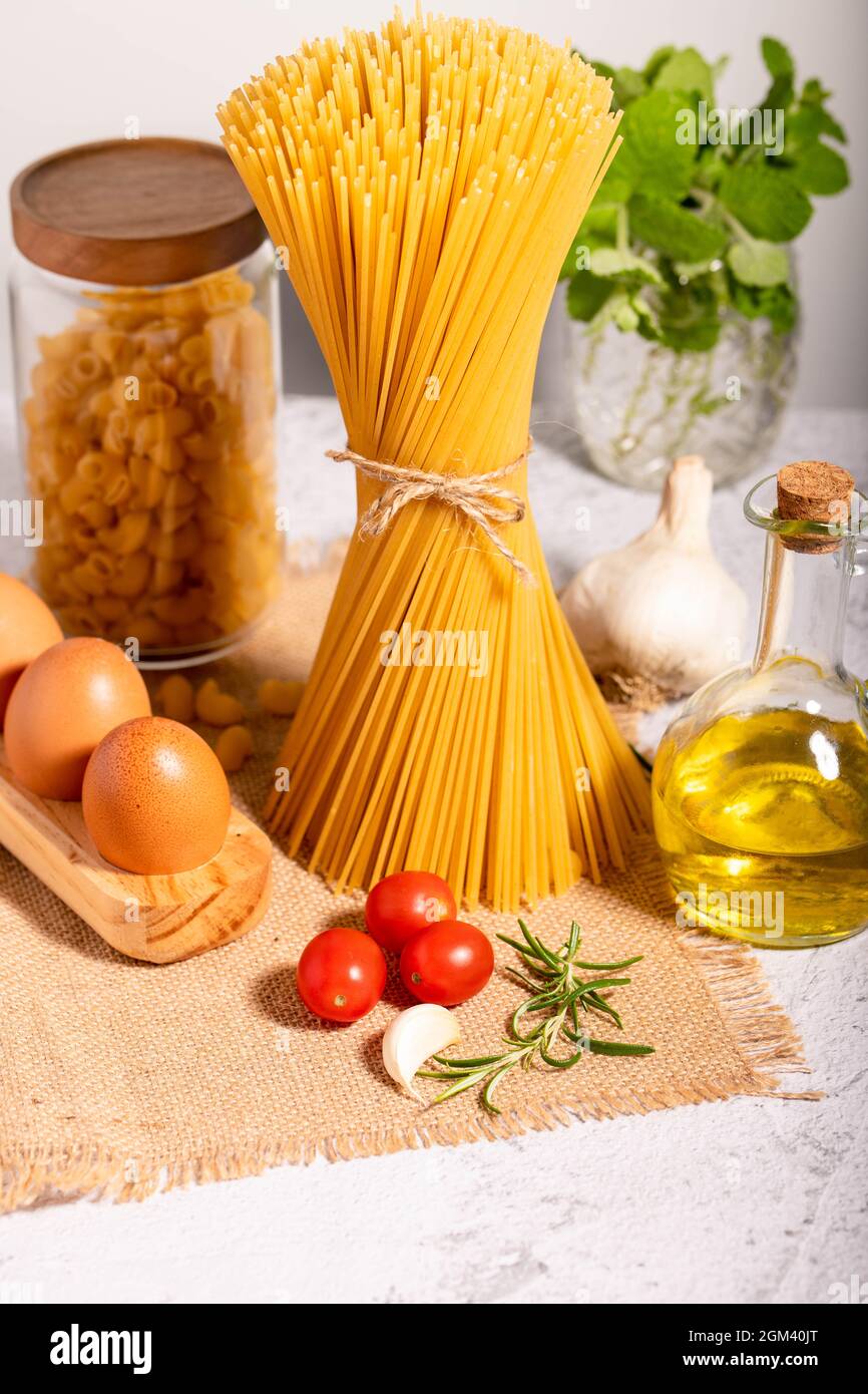 Carbo-Diät - Spaghetti, Ditalini rohe Pasta zusammen mit einem Glas Olivenöl, cherri Tomaten, Knoblauch und Eier in Öko-Holz-Palette. Stockfoto