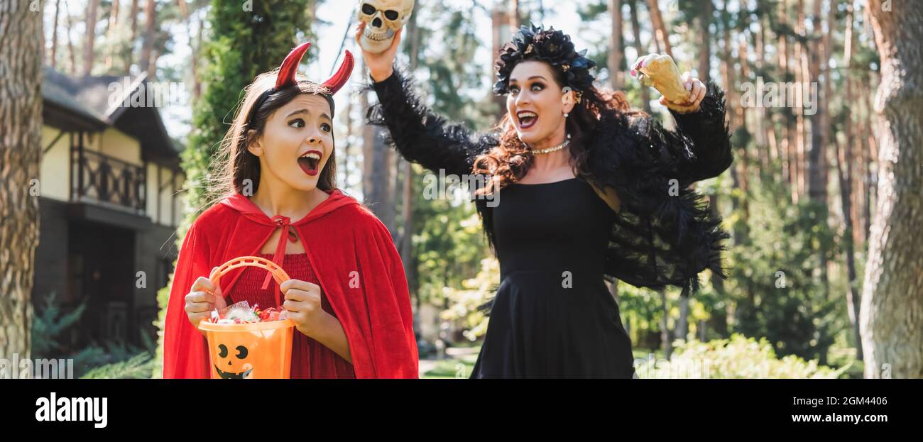 Frau im Vampir halloween Kostüm erschreckt Tochter mit Spielzeug Hand und Schädel, Banner Stockfoto