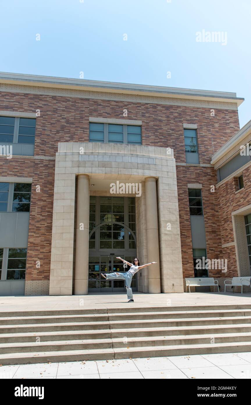 Selbstbewusste Schülerin auf dem College-Campus balancierte auf einem Bein, während sie sich vor dem Backsteingebäude zurücklehnte. Stockfoto