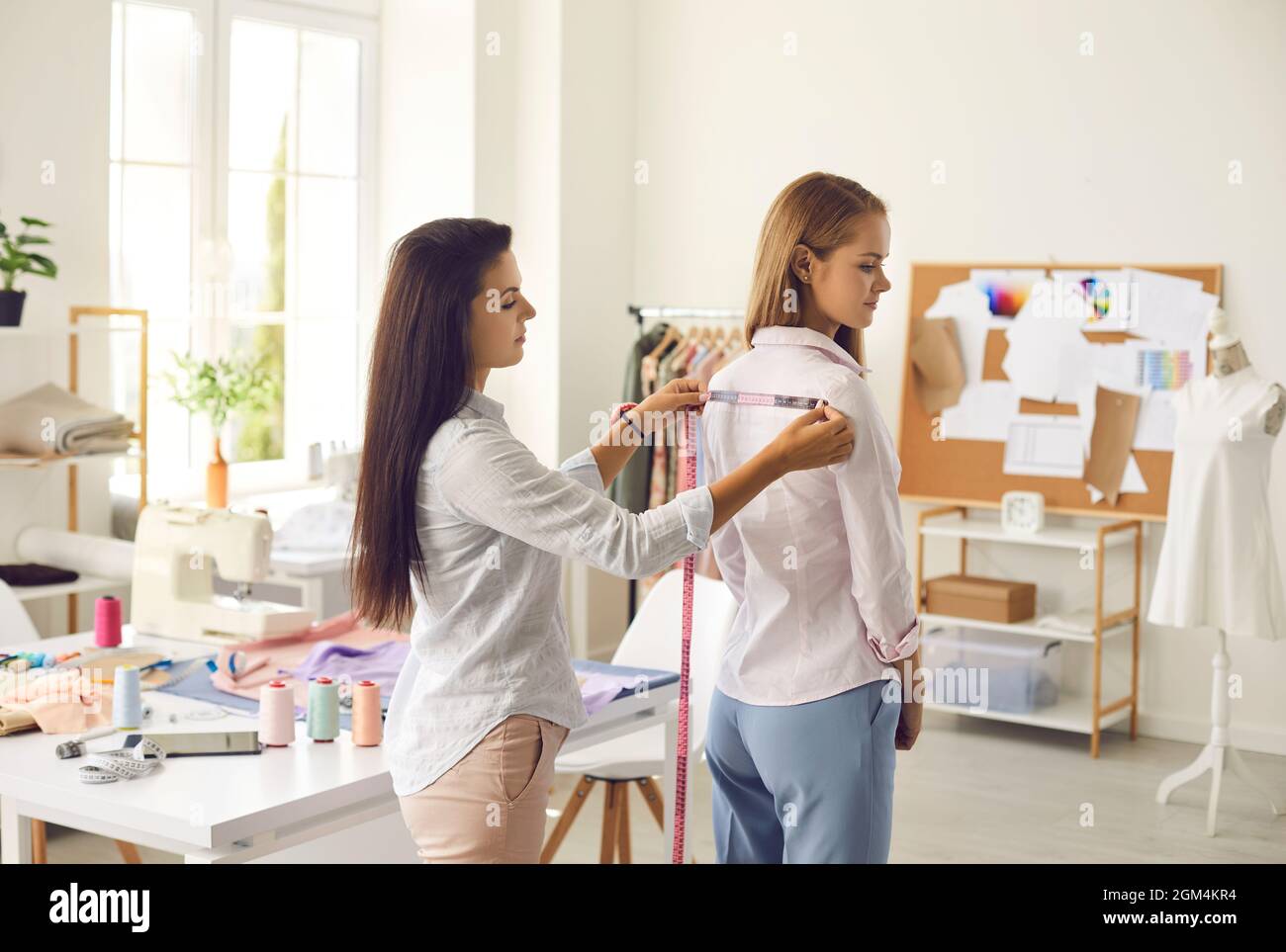 Schneiderin, die mit ihrem Maßband die Schultern einer Frau misst Stockfoto