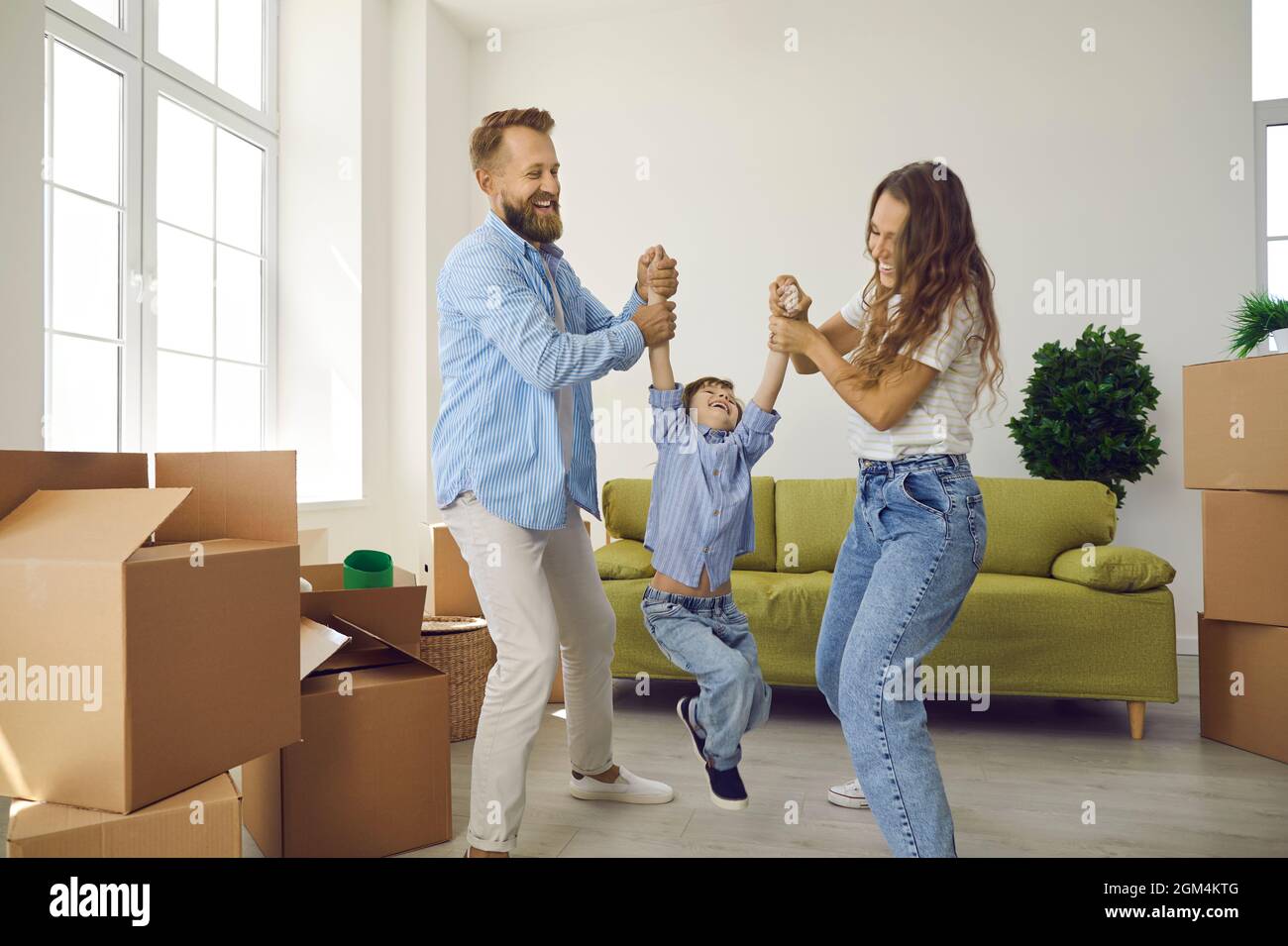 Glückliches junges Paar mit Kind, das am Umzugstag Spaß im Wohnzimmer in ihrem neuen Zuhause hat Stockfoto