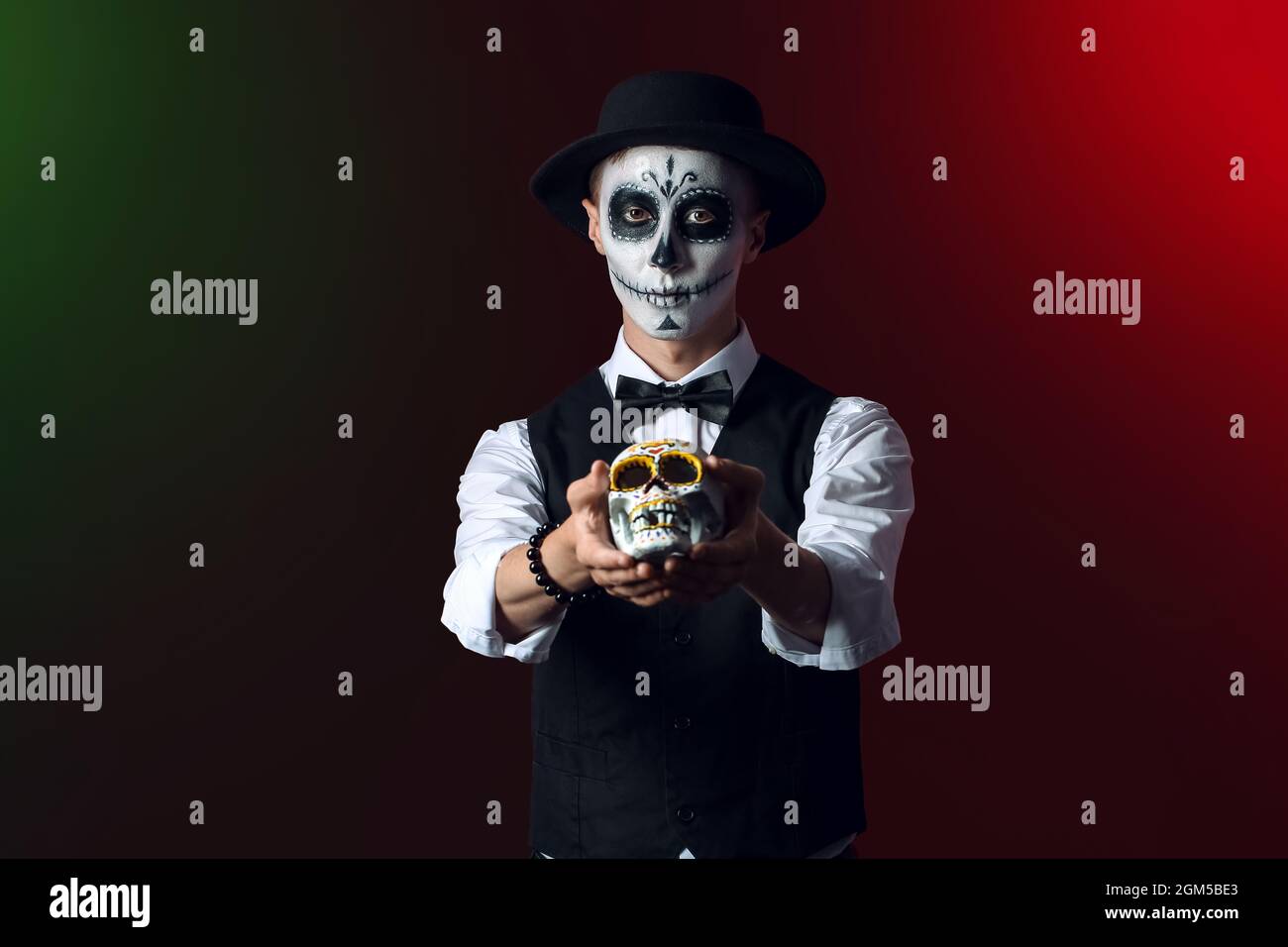 Junger Mann mit gemaltem Gesicht und Zuckerschädel für Mexikos Tag der Toten (El Dia de Muertos) auf dunklem Hintergrund Stockfoto
