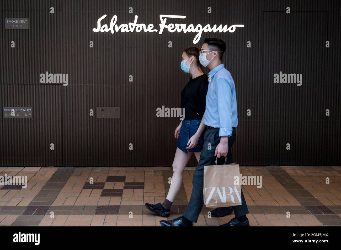 Ein Paar mit einer Zara-Einkaufstasche geht an dem italienischen Luxusschuhladen Salvatore Ferragamo mit Logo in Hongkong vorbei. Stockfoto