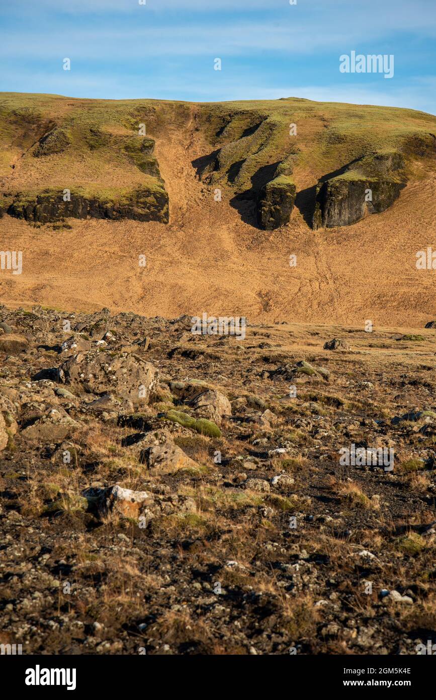 Isländische Topographie mit warmen Braun- und Orange-Tönen und felsiger Struktur mit blauem Himmel Stockfoto