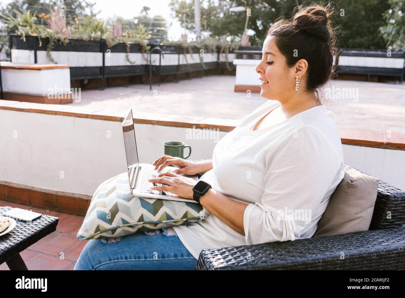 Molliges lateinisches Mädchen, das am Computer auf der Terrasse in Lateinamerika sitzt Stockfoto