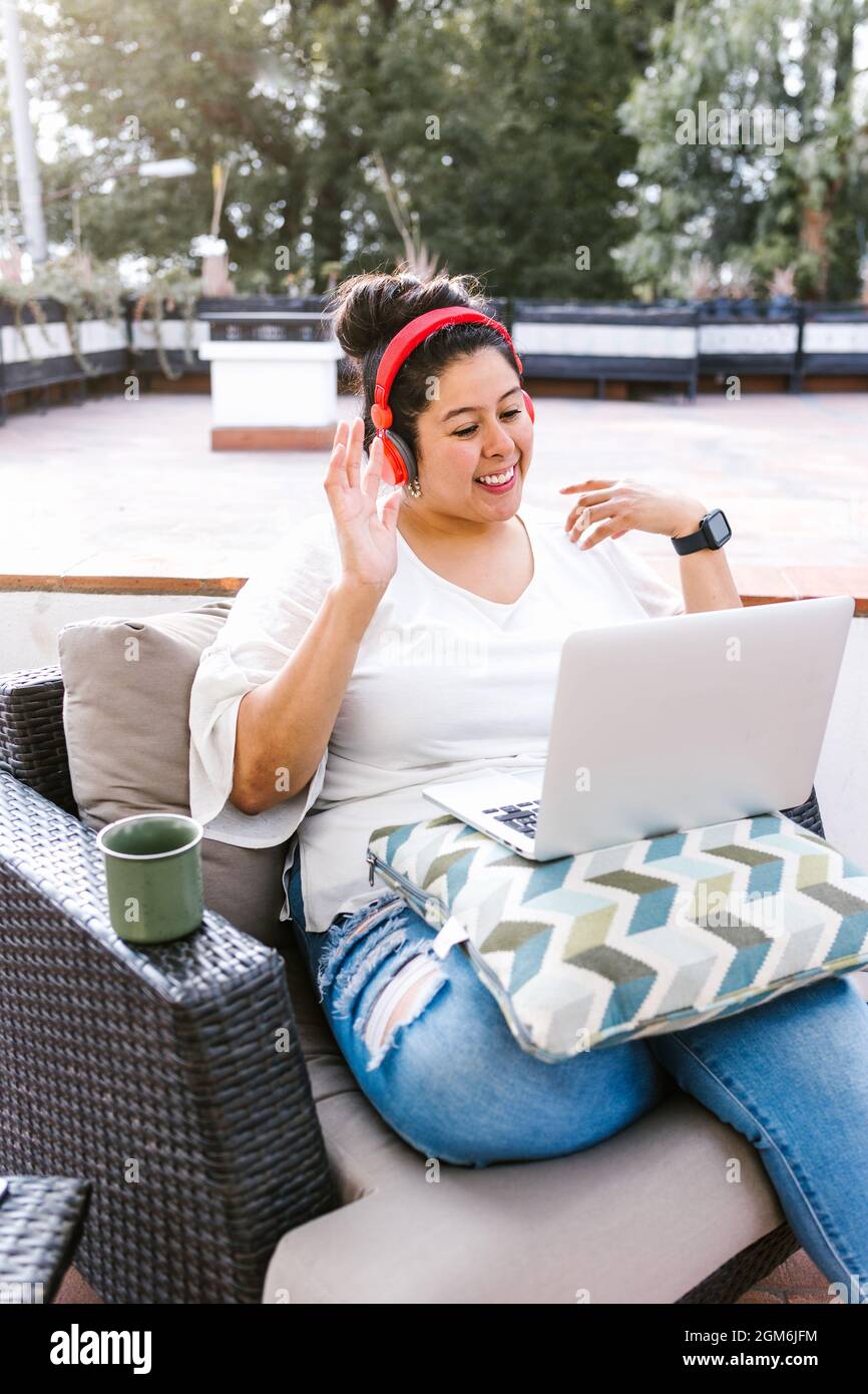 Junge kurvige lateinerin mit Computer, die Videoanruf macht, sitzt auf der Terrasse in Lateinamerika Stockfoto