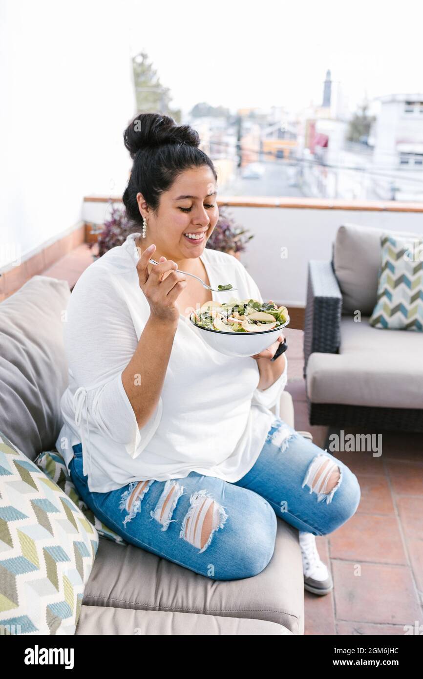 Junge kurvige Mexikanerin, die auf der Terrasse in Lateinamerika Salat isst Stockfoto