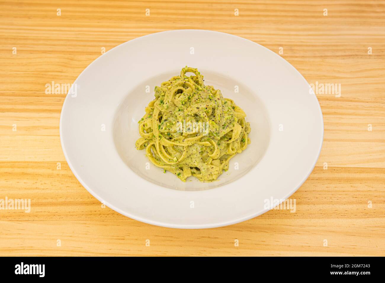 Italienische Tagliatelle Pasta Rezept mit Pesto und Pistazien-Sauce auf weißem Teller und gelbem Holztisch Stockfoto