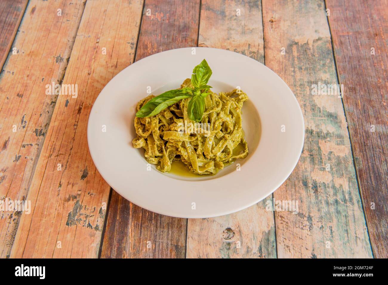Grüne Gemüsepasta Tagliatelle mit italienischer Pesto-Sauce mit Nüssen und Basilikumblättern auf dem Holztisch Stockfoto
