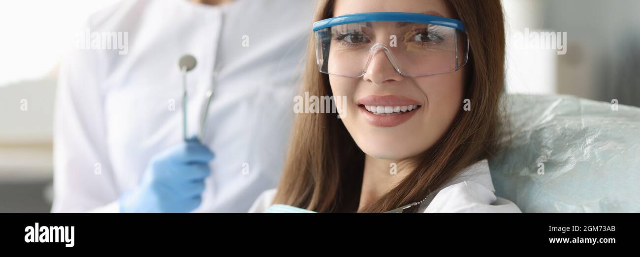 Frau Patientin in einer Sicherheitsbrille, die in einem Zahnarztstuhl in der Nähe sitzt Arzt Stockfoto Frau Patientin in einer Sicherheitsbrille, die in einem Zahnarztstuhl in der Nähe sitzt Arzt Stockfoto