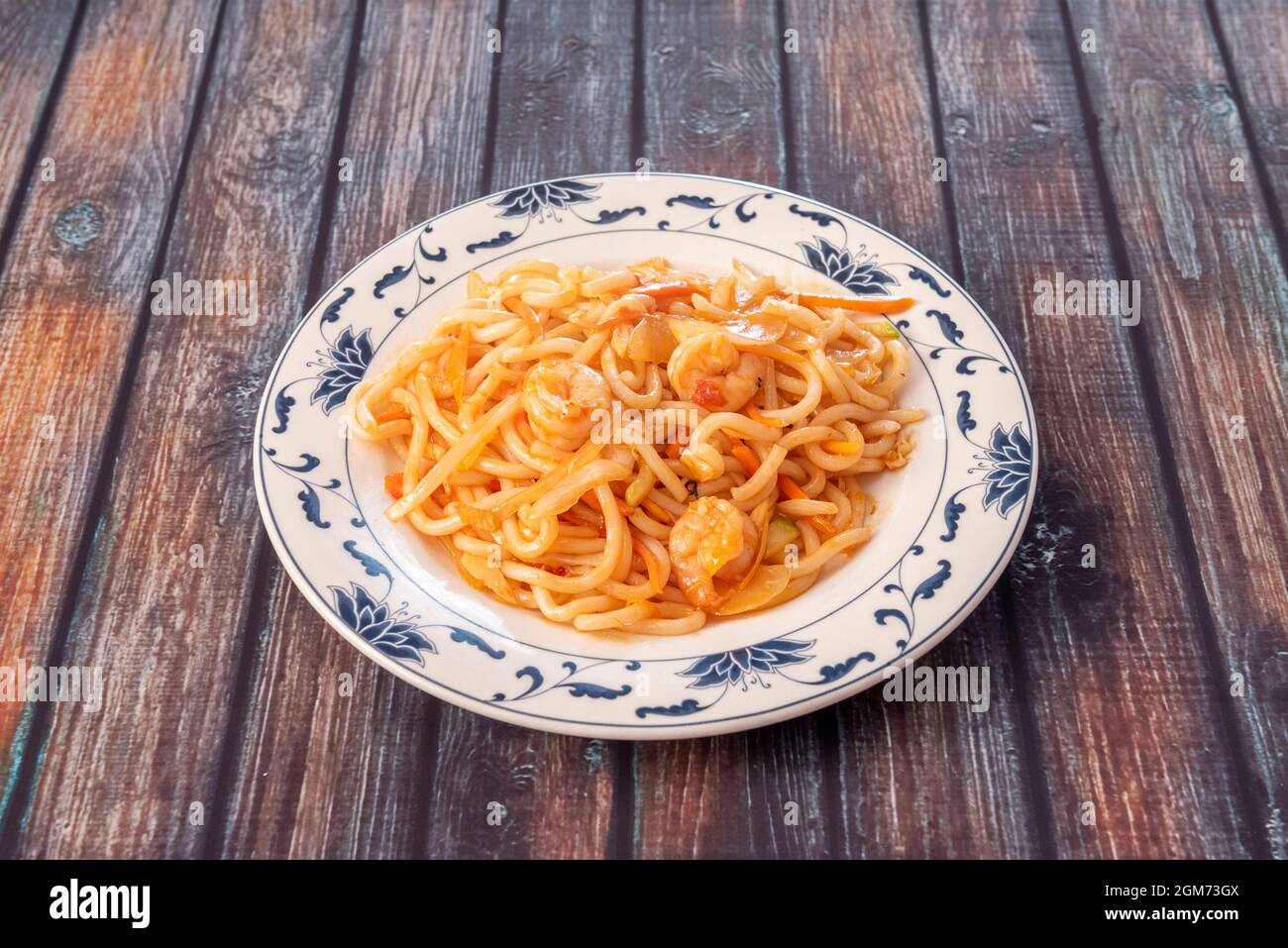 Teller mit udon-Nudeln, die in einem chinesischen Restaurant mit Garnelen, Zwiebeln und Gemüse sautiert werden. Stockfoto