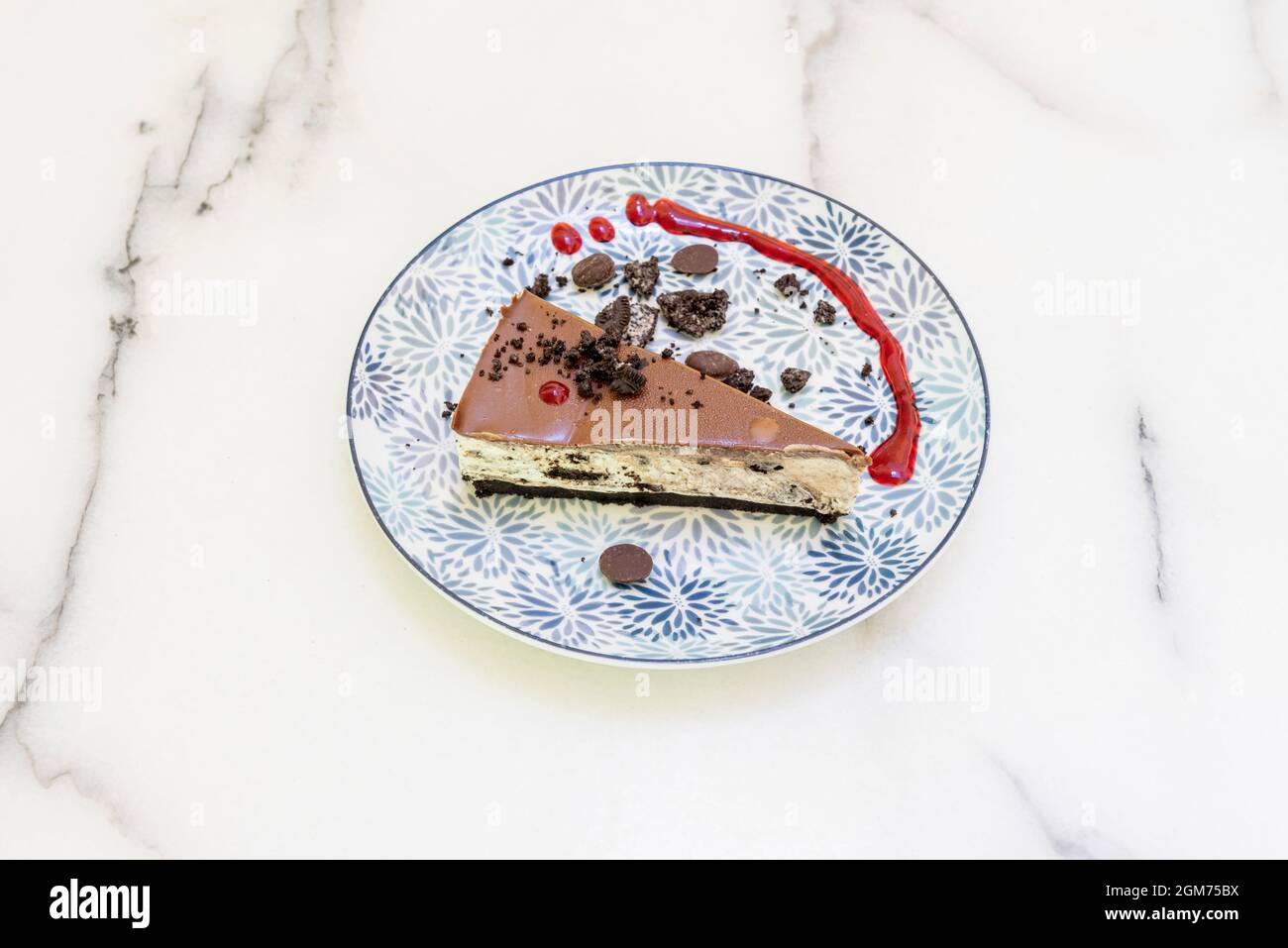 oreo-Kuchen mit Schokoladenstückchen und rotem Fruchtsirup auf weißem Marmortisch Stockfoto