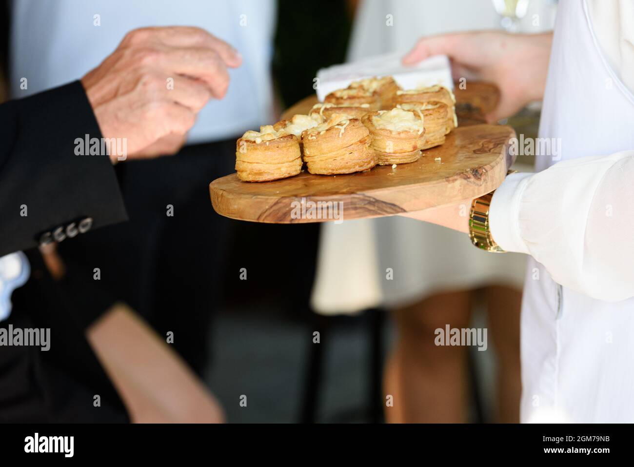 Eine handtake Vorspeise mit einer Käsefüllung auf einem Holzteller, die von einem Kellner in einer weißen Weste gehalten wird Stockfoto
