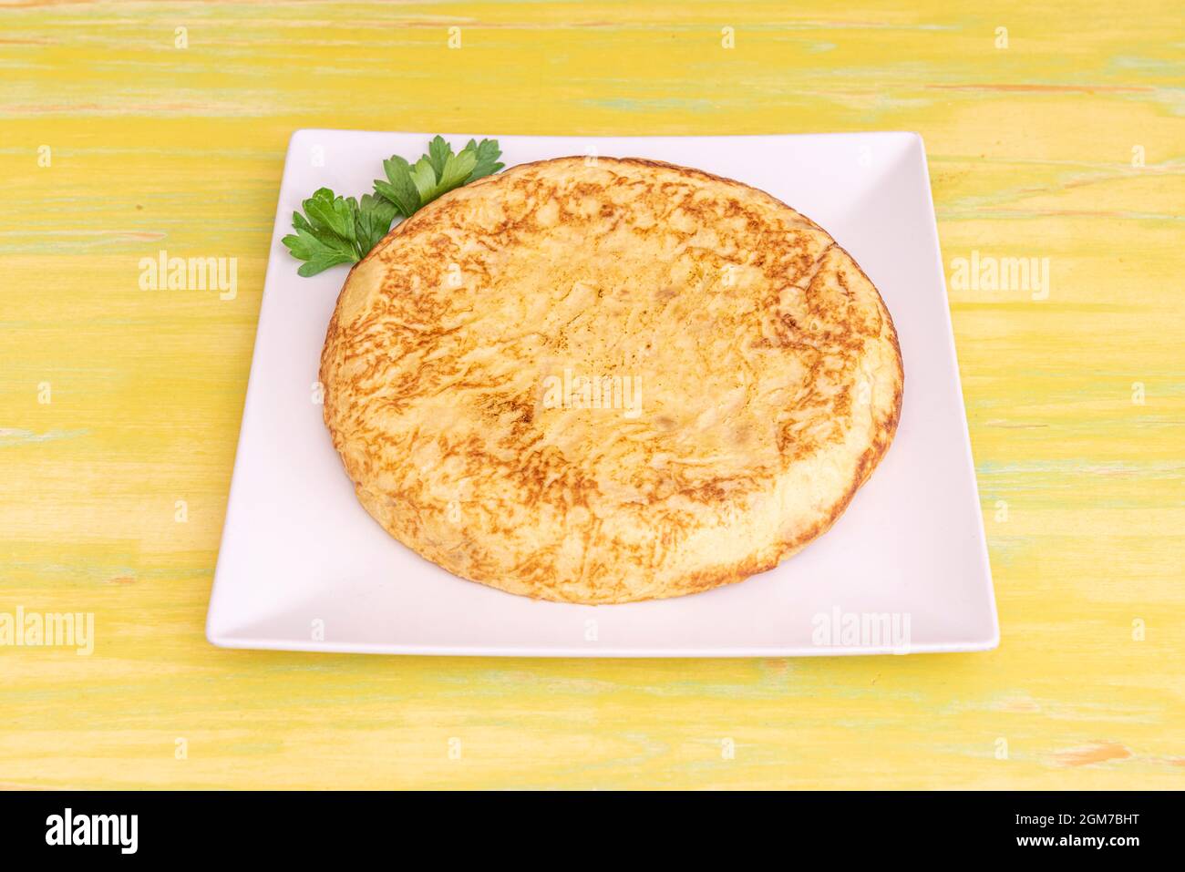 Omelette mit Kartoffeln und Eiern auf einem weißen quadratischen Teller auf einem gelben Holztisch serviert Stockfoto
